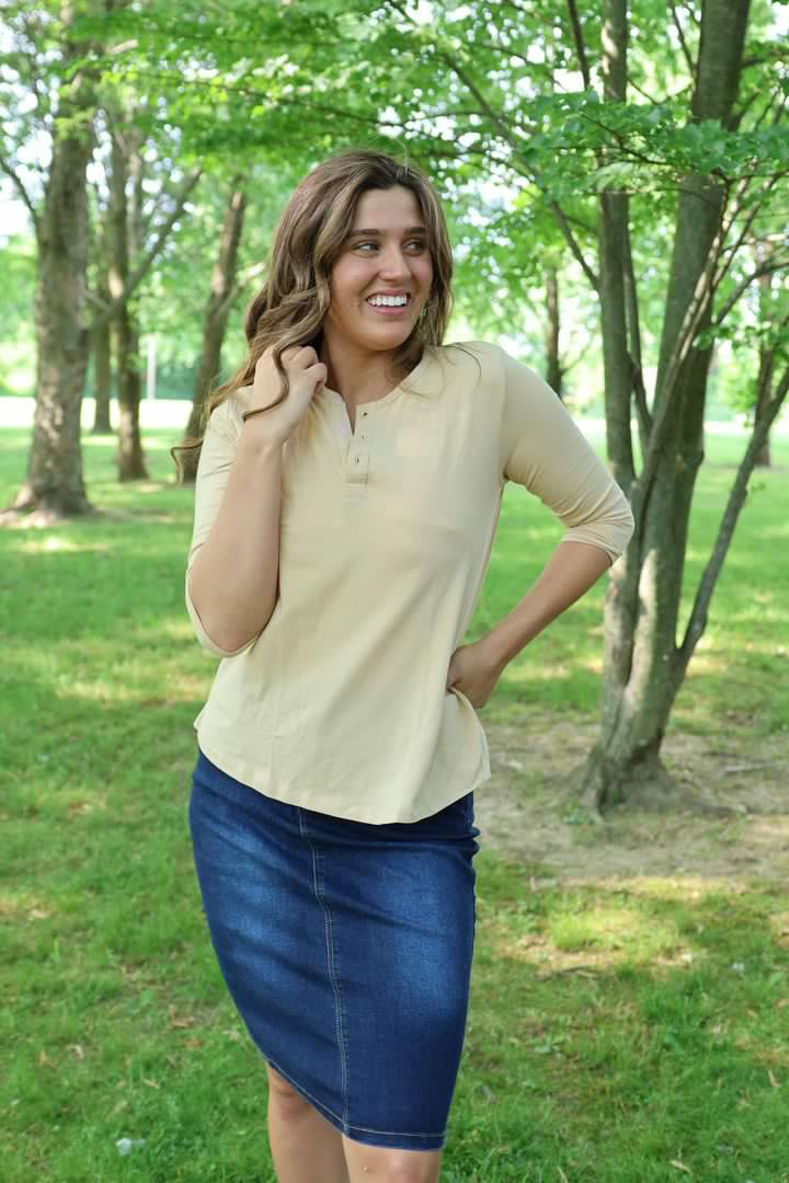 woman wearing a tan colored top with 3 buttons and a denim jean skirt